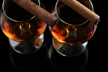 two glasses of brandy and cigars on black background