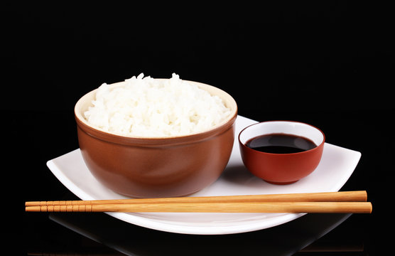 Bowl of rice and chopsticks on plate isolated on black