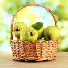 sweet quinces with leaves in basket, on green background