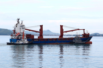 Tugboat assisting bulk cargo ship to harbor quayside