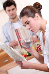 Woman drinking a glass of water and reading the paper