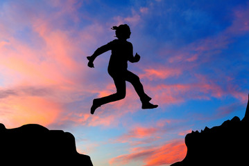 Silhouette of hiking woman jumping over the mountains at sunset