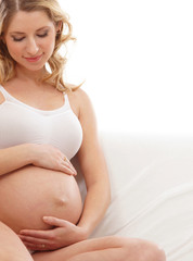 Fototapeta na wymiar Młodych blond kobieta w ciąży siedzi w białej bieli¼nie