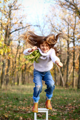 Happy little girl jumping from a chair outdoors