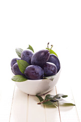 Fresh plums in a bowl with green leaves