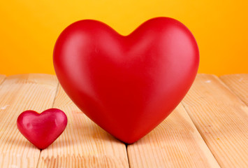 Decorative red hearts on wooden table on orange background