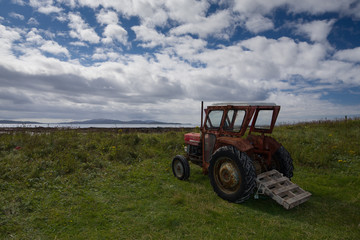 Obraz premium Rusty old red tractor by the sea