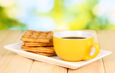 Cup of coffee and cookies on wooden table on bright background