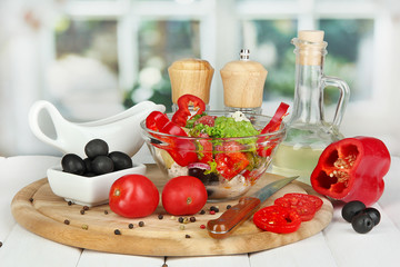 Fresh greek salad in glass bowl surrounded by ingredients for