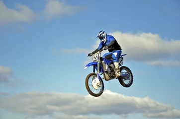 Foto op Plexiglas Vlucht van motorcrosser tegen de blauwe lucht en de wolken © VVKSAM