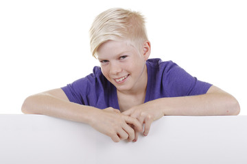 Blonder Junge schaut lächelnd über ein leeres Plakat