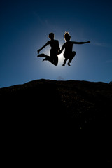 silhouette of couple jumping on top of hill
