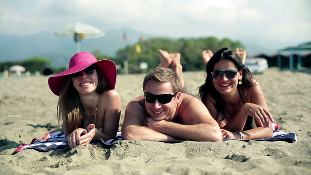 Three young people lying on sand and looking at camera