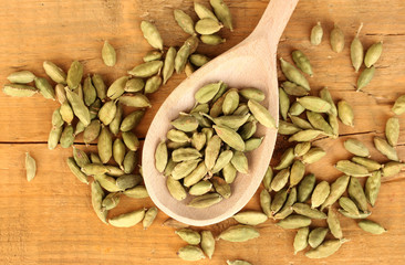 green cardamom in wooden spoon on wooden background close-up