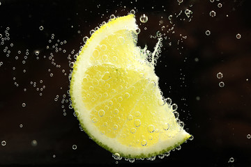 slice of lime in the water with bubbles, on black background