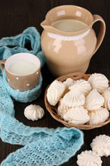 Obraz na płótnie Canvas Pitcher and cup of milk with meringues on wooden table close-up