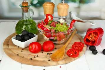 Fresh greek salad in glass bowl surrounded by ingredients for