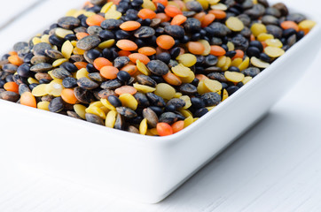 Variety lentils in porcelain plate on white table close up