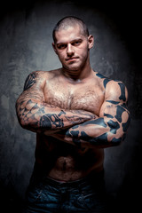 Muscular young man with many tattoos posing over grey background