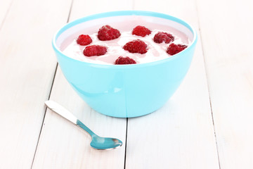 Yogurt with raspberries in bowl on wooden background
