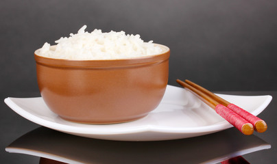 Bowl of rice and chopsticks on plate on grey background