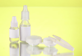 Eye drop and lenses on green background