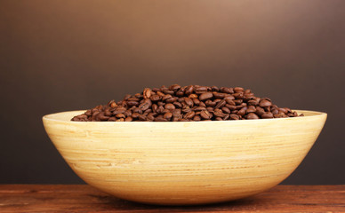 Coffee beans in bamboo bowl on table on brown background