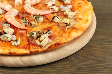 Delicious pizza with seafood on stand on wooden background