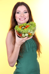 Beautiful woman with vegetable salad on yellow background