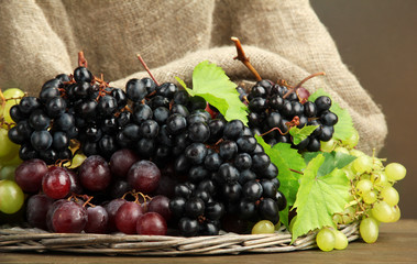 assortment of ripe sweet grapes in basket, on brown background