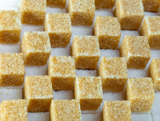 Cubes of not refined reed sugar lie on pieces of white sugar..