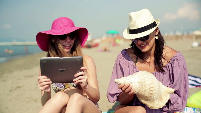 Girlfriends taking photo of seashell with tablet on the beach