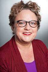 Smiling senior woman with short curly hair. Wearing glasses.