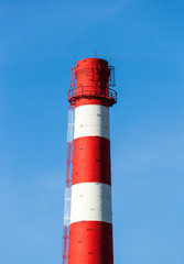 Red and white factory chimney against blue sky