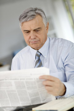 Senior businessman reading newspaper with puzzled look