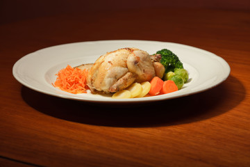 Dinner of vegetables and chicken on a plate and wooden table.