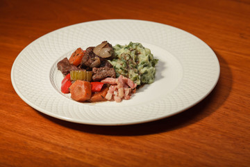 Dinner of vegetables potatoes and meat on a white plate.