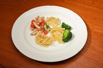 Dinner of vegetables pasta tomato and chicken on a white plate.