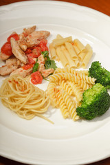 Dinner of vegetables pasta tomato and chicken on a white plate.