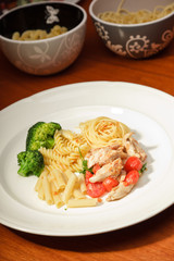 Dinner of vegetables pasta tomato and chicken on a white plate.