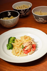 Dinner of vegetables pasta tomato and chicken on a white plate.