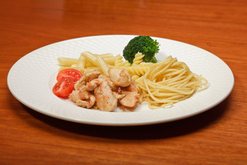 Dinner of vegetables pasta tomato and chicken on a white plate.