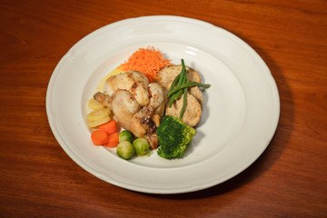 Dinner of vegetables and chicken on a plate and wooden table.