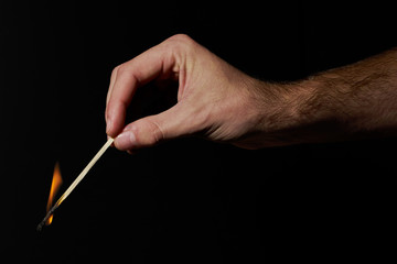 Hand holding burning match stick on black background