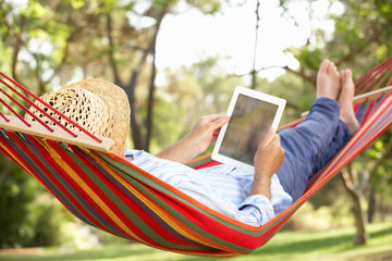 Senior Man Relaxing In Hammock With  E-Book
