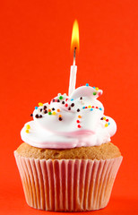 tasty birthday cupcake with candle, on red background