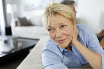 Senior woman sitting in couch, husband in background