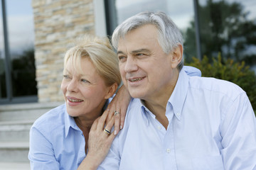 Senior couple sitting in front of house and looking away