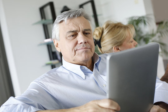 Senior man reading news on tablet sitting in couch