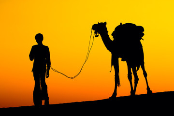 Silhouette of a man and camel at sunset in the desert, India
